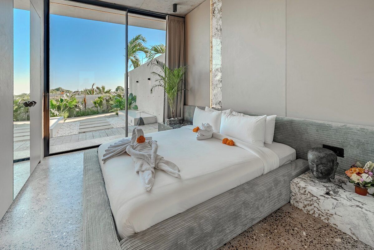 A modern hotel room with a large bed, a view of palm trees, and a marble accent wall.