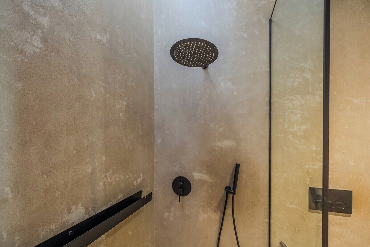 A shower area with a handheld showerhead and a wall-mounted control panel.