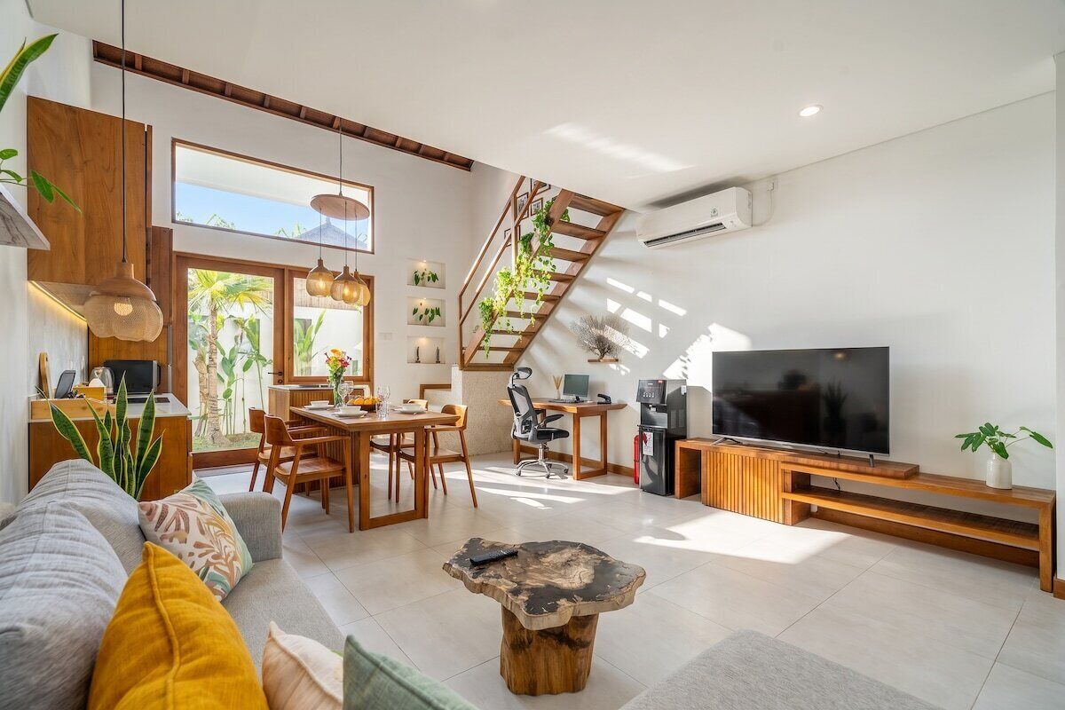 A modern living room with a sofa, coffee table, TV, and a staircase with plants.