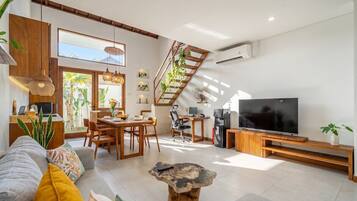 A modern living room with a sofa, coffee table, TV, and a staircase with plants.