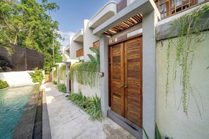 A modern building with a swimming pool, wooden doors, and a garden area. - Cozy 1BR Townhouse w 2 Pools, Patio & Private Yard (Kuta Utara)