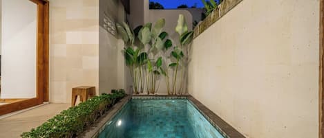 A rectangular swimming pool with a tiled edge, surrounded by a low stone wall and a wooden bench.