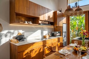 A modern kitchen with wooden cabinetry, a built-in microwave, and a dining area with a table set for two. - Cozy 1BR Townhouse w 2 Pools, Patio & Private Yard (Kuta Utara)