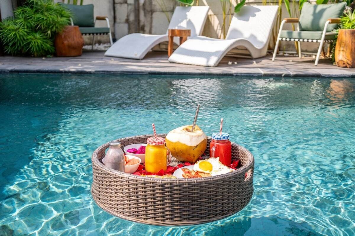 A poolside setting with a wicker tray containing a drink, a coconut, and a plate with food.