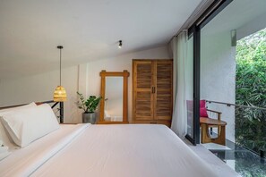 A bedroom with a large bed, a bedside lamp, a wooden wardrobe, and a balcony with a view of greenery. - Serene 1BR Flat in Ubud's Centre • Pool • Kitchen (Gianyar Regency)