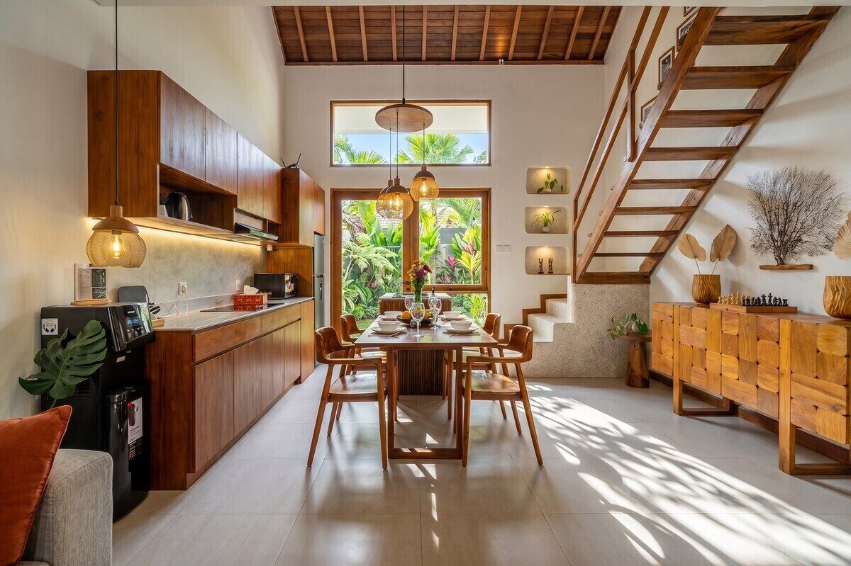 A modern kitchen with wooden cabinets, a dining table set for six, and a staircase leading to an upper level.
