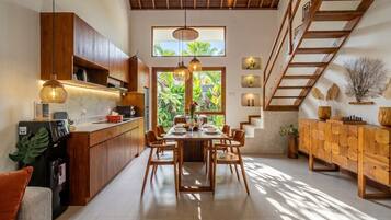 A modern kitchen with wooden cabinets, a dining table set for six, and a staircase leading to an upper level.