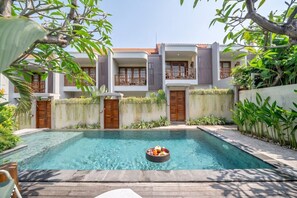 A swimming pool with a floating bar, surrounded by a building with balconies and a garden. - Cozy 1BR Townhouse w 2 Pools, Patio & Private Yard (Badung Regency)