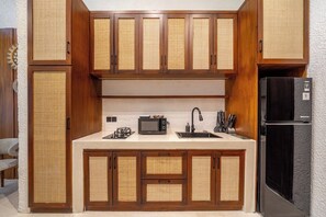 A compact kitchen with wooden cabinets, a microwave, a sink, and a refrigerator. - Cozy 1BR Flat in Ubud • Pool • Kitchen • Garden (Gianyar Regency)