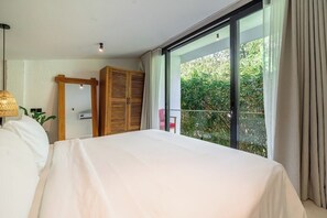 A bedroom with a large bed, a wardrobe, and a sliding glass door leading to a balcony with greenery outside. - Cozy 1BR Flat in Ubud • Pool • Kitchen • Garden (Gianyar Regency)