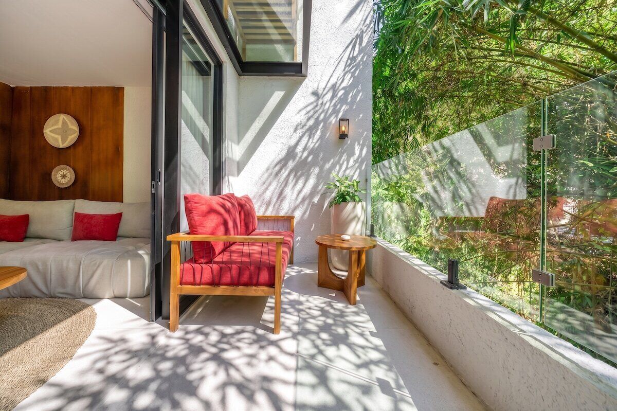 Un balcón moderno con un sofá, una silla roja y una mesita.