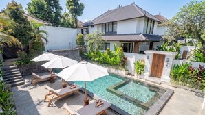 A pool area with lounge chairs and umbrellas, surrounded by a white wall and greenery. - Chic 1BR in Tropical Ubud • Pool • Kitchen • Patio (Gianyar Regency)
