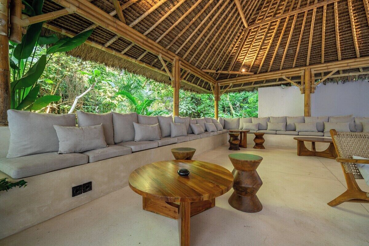 A covered outdoor seating area with a sofa and round tables.
