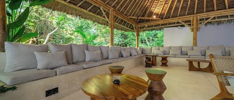 A covered outdoor seating area with a sofa and round tables.