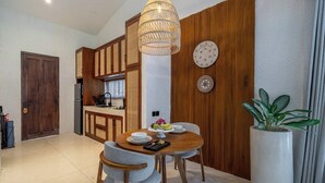 A dining area with a round table, chairs, a hanging light fixture, and a potted plant. - Chic 1BR in Tropical Ubud • Pool • Kitchen • Patio (Gianyar Regency)