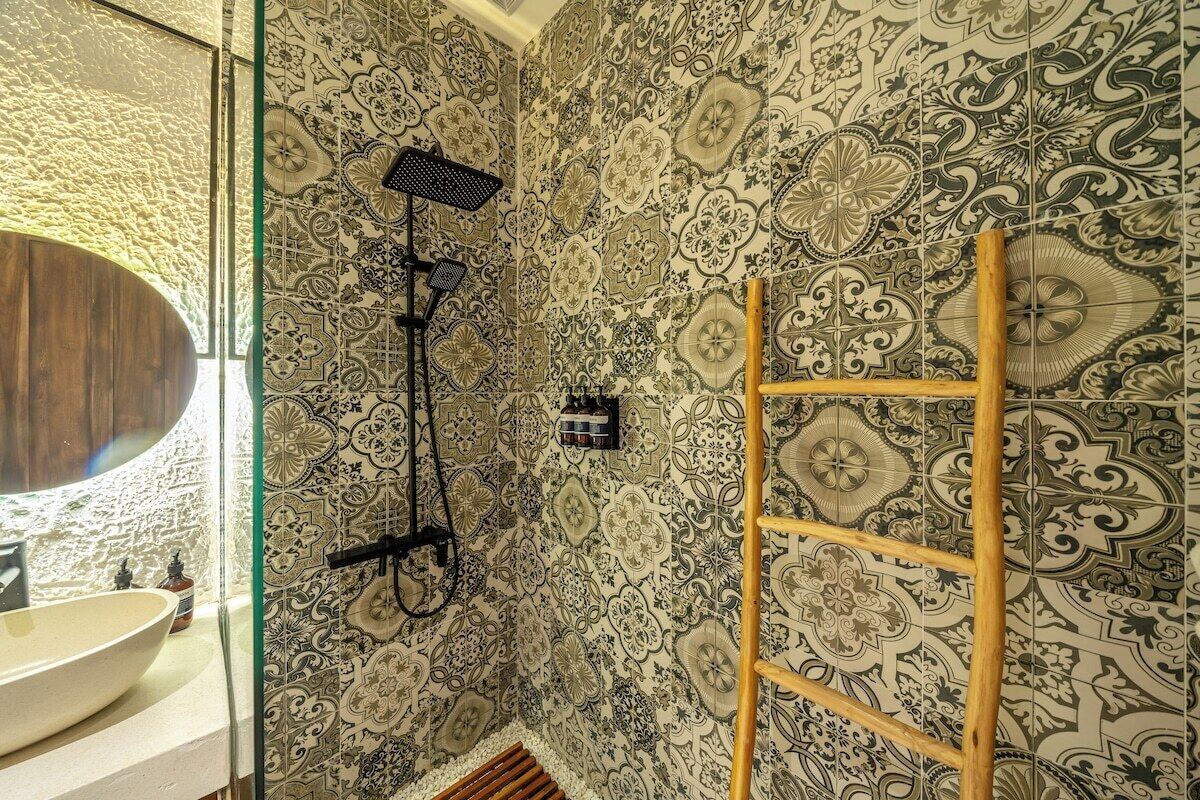 Casa de banho com parede de azulejos estampados, escada de madeira, chuveiro e lavatório com espelho.