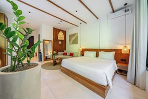 A modern hotel room with a large bed, a seating area, a potted plant, and a wall-mounted air conditioner. - Stylish 1BR in Ubud w Pool, Patio, Private Kitchen (Gianyar Regency)