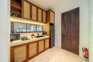 A compact kitchen with wooden cabinets, a built-in microwave, a sink, and a refrigerator. - Stylish 1BR in Ubud w Pool, Patio, Private Kitchen (Gianyar Regency)