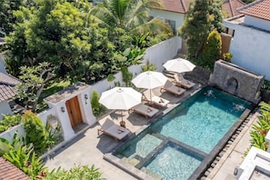 A swimming pool with lounge chairs and umbrellas, surrounded by greenery and a white wall. - Stylish 1BR in Ubud w Pool, Patio, Private Kitchen (Gianyar Regency)