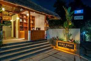 A hotel entrance with a thatched roof, wooden reception desk, and a sign reading 'Sacred Jungle'. - Stylish 1BR in Ubud w Pool, Patio, Private Kitchen (Gianyar Regency)