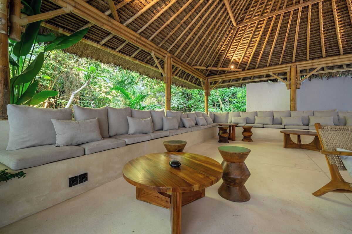 An indoor seating area with a thatched roof, cushioned sofas, and wooden tables.