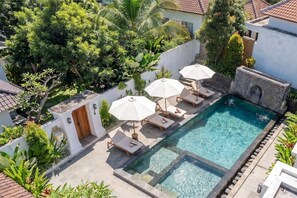 Piscina com espreguiçadeiras e guarda-sóis, cercada por vegetação e uma parede branca.