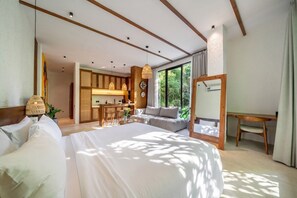 Quarto de hotel moderno com cama grande, escrivaninha e sofá. Há vista para o verde lá fora.