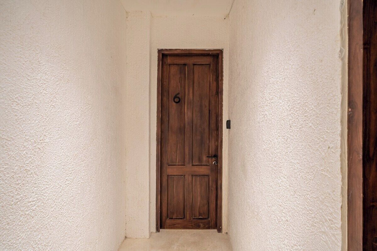 A wooden door with a number '6' on it, set in a narrow hallway with textured walls.