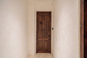 Uma porta de madeira com o número 6, em um corredor estreito com paredes texturizadas.