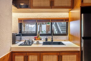 A compact kitchen with a built-in gas stove, a sink, and a window with blinds. - Tropical 1BR Stay in Ubud w Pool, Patio & Kitchen (Gianyar Regency)