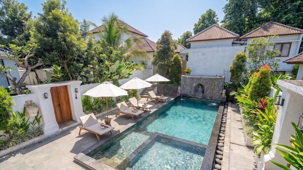 A swimming pool with lounge chairs and umbrellas, surrounded by greenery and buildings. - Best 1BR Stay in Ubud • Pool • Garden • Kitchen (Gianyar Regency)