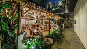 An outdoor patio area with a covered seating area, stone walls, and lush greenery. - Best 1BR Stay in Ubud • Pool • Garden • Kitchen (Gianyar Regency)
