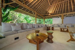 Ein Sitzbereich im Innenbereich mit einem Reetdach, gepolsterten Sofas und Holztischen.