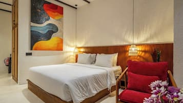 A bedroom with a bed, a red chair, a wall painting, and a wall-mounted lamp.