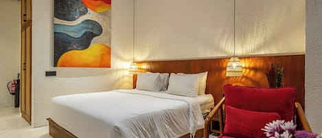 A bedroom with a bed, a red chair, a wall painting, and a wall-mounted lamp.