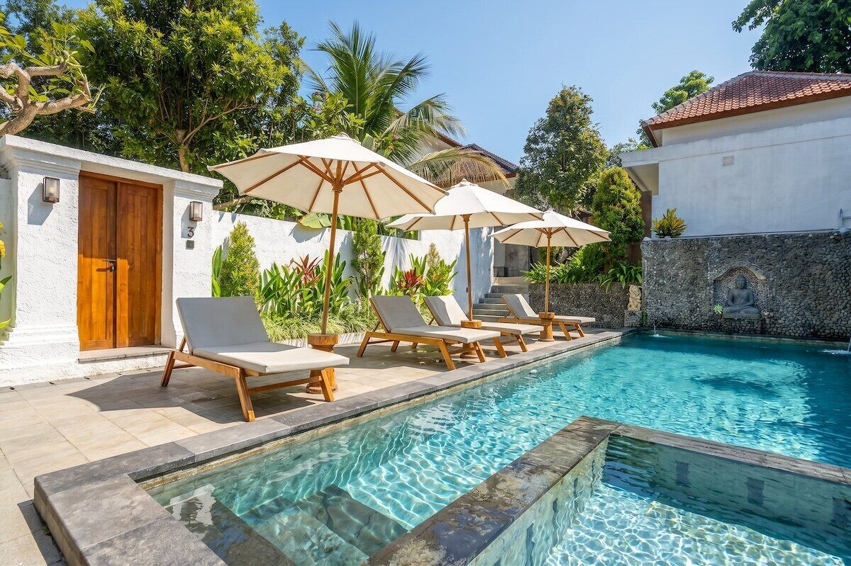 A pool area with lounge chairs and umbrellas, a stone wall, and a wooden door.