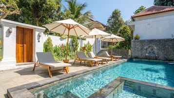 A pool area with lounge chairs and umbrellas, a stone wall, and a wooden door.