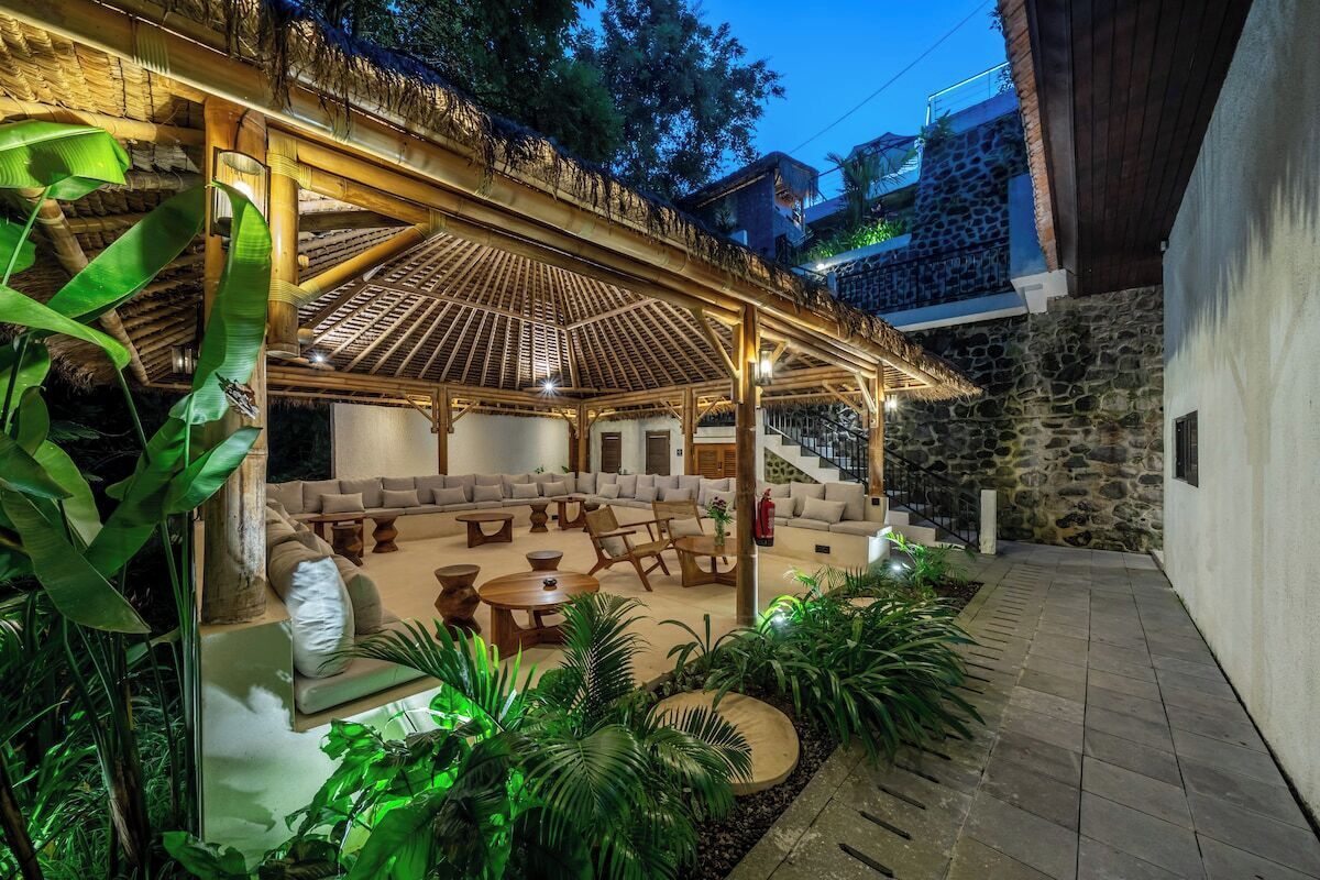 An outdoor lounge area with a covered seating arrangement, stone walls, and lush greenery.