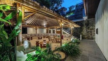 An outdoor lounge area with a covered seating arrangement, stone walls, and lush greenery.