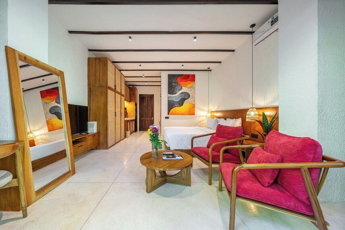 Een hotelkamer met een bed, een zithoek met een rode bank, een bijzettafeltje en een spiegel.