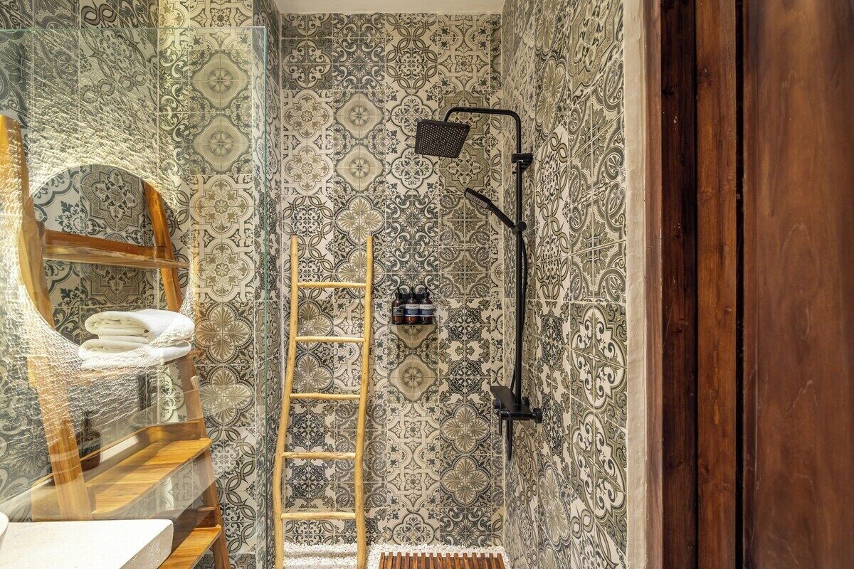 Casa de banho com azulejos estampados, uma escada de madeira, um porta-toalhas e um chuveiro com chuveiro manual.
