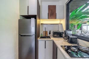 A compact kitchen with a stainless steel refrigerator, a built-in microwave, a gas stove, and a window with a view of greenery. - Cozy 1BR in Central Ubud • Pool • Patio • Kitchen (Ubud)