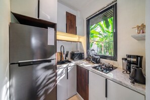 A compact kitchen with a stainless steel refrigerator, a microwave, a coffee maker, and a window with a view of greenery. - Cozy 1BR in Central Ubud • Pool • Patio • Kitchen (Ubud)