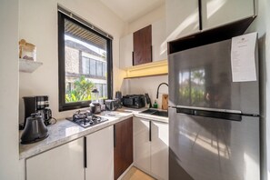 A compact kitchen with a built-in stove, a refrigerator, and a window with a view of greenery outside. - Best Ubud's 1BR w Pool, Patio & Private Kitchen (Kabupaten Gianyar)