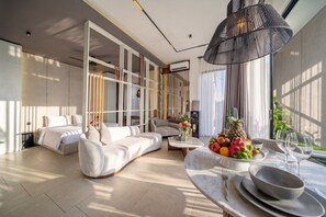 A modern living room with a sofa, a dining table set with plates and glasses, and a fruit bowl. - Best Ubud's 1BR w Pool, Patio & Private Kitchen (Kabupaten Gianyar)