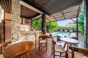An outdoor pool area with wooden furniture and a stone wall. - Best Ubud's 1BR w Pool, Patio & Private Kitchen (Kabupaten Gianyar)