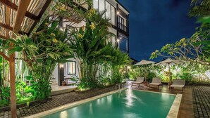 Et poolområde med liggestole og en bygning i baggrunden.