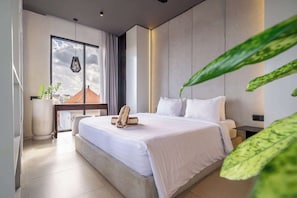 A modern bedroom with a large bed, a bedside table, a lamp, and a view through a window. - Best Ubud's 1BR Apartment w Pool, Patio & Kitchen (Ubud)