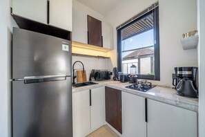 A compact kitchen with a stainless steel refrigerator, a coffee maker, and a window providing natural light. - Best Ubud's 1BR Apartment w Pool, Patio & Kitchen (Ubud)