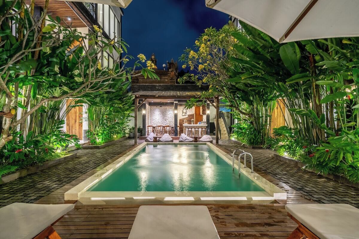 A swimming pool with a wooden deck, surrounded by lush greenery and a covered seating area.